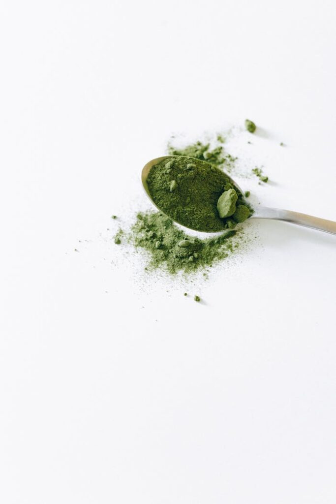 Top view of organic matcha powder on a silver spoon with a white background.